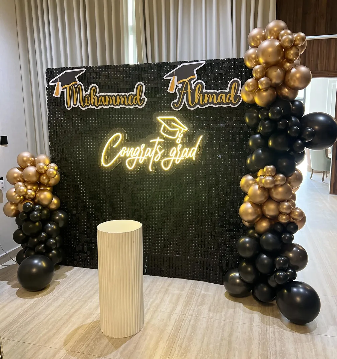 Black and gold graduation photo wall with illuminated names and balloon clusters