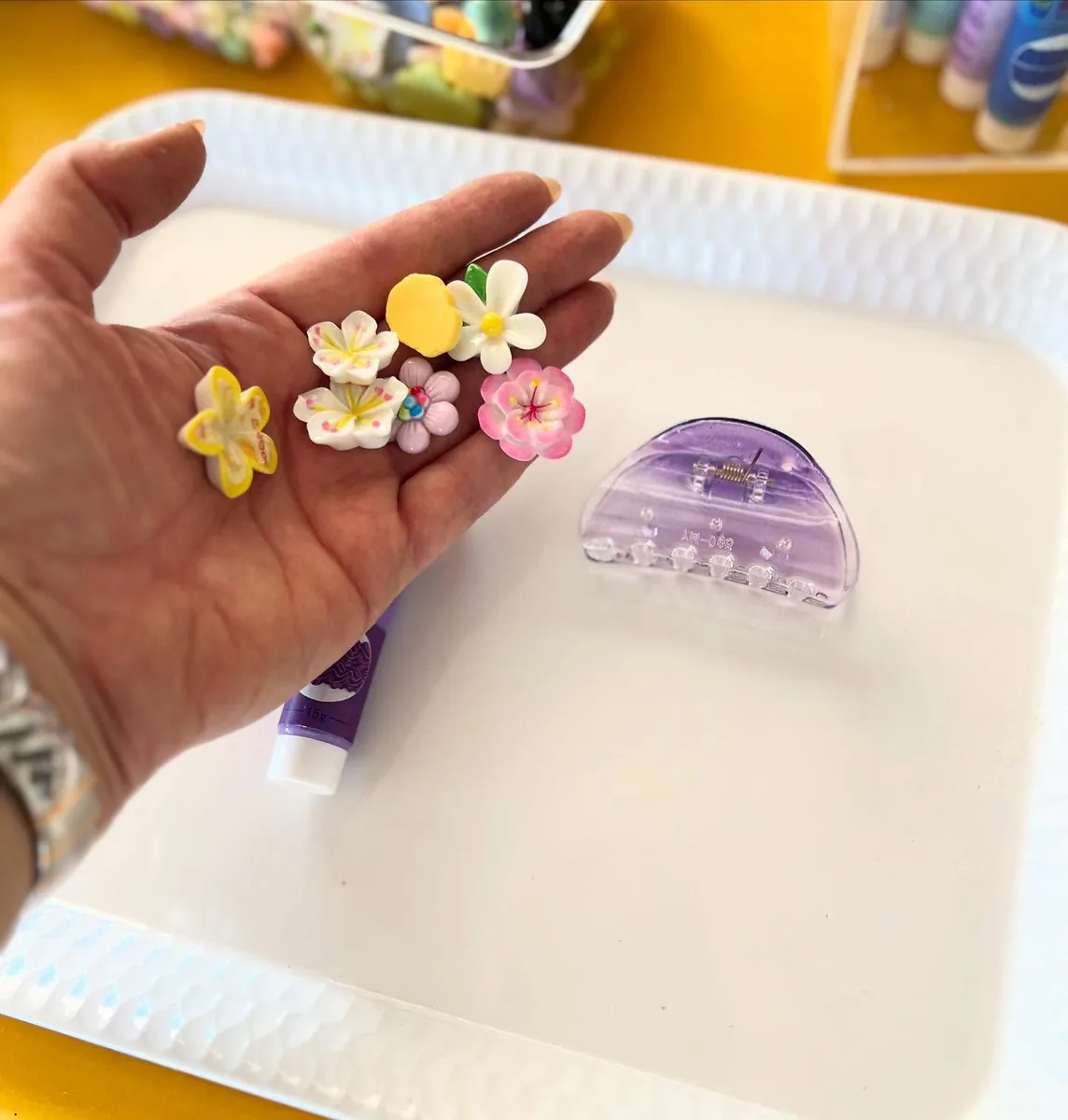 Small handmade floral hair clips displayed in a hand beside craft materials