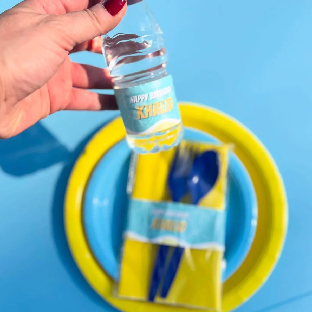 Small water bottle with a personalized summer birthday label beside yellow and blue tableware