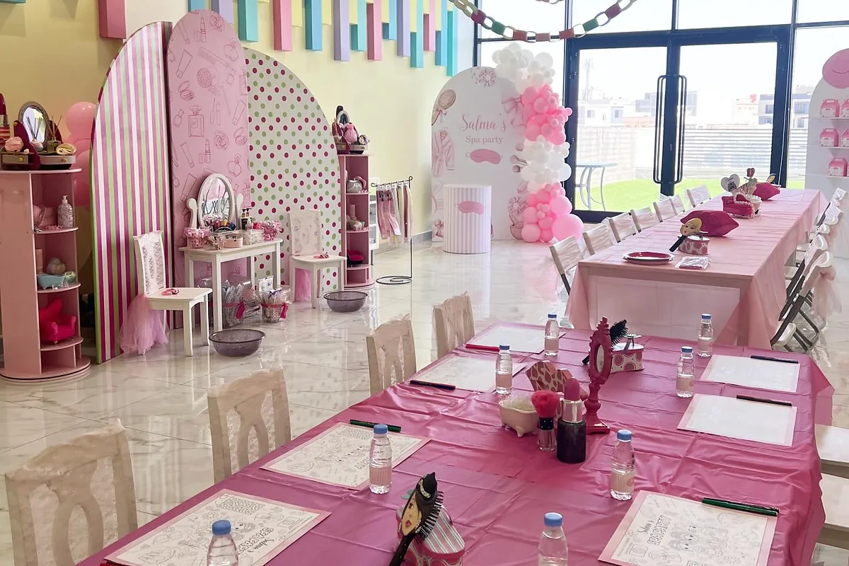 Pink spa birthday room with long children’s table, beauty stations and party seating
