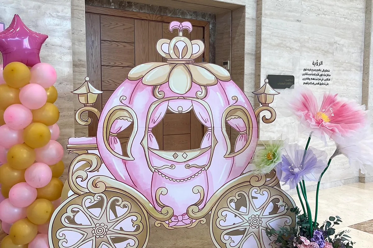 عربة أميرة وردية كبيرة بجانب بالونات وزهور عند مدخل الحفل