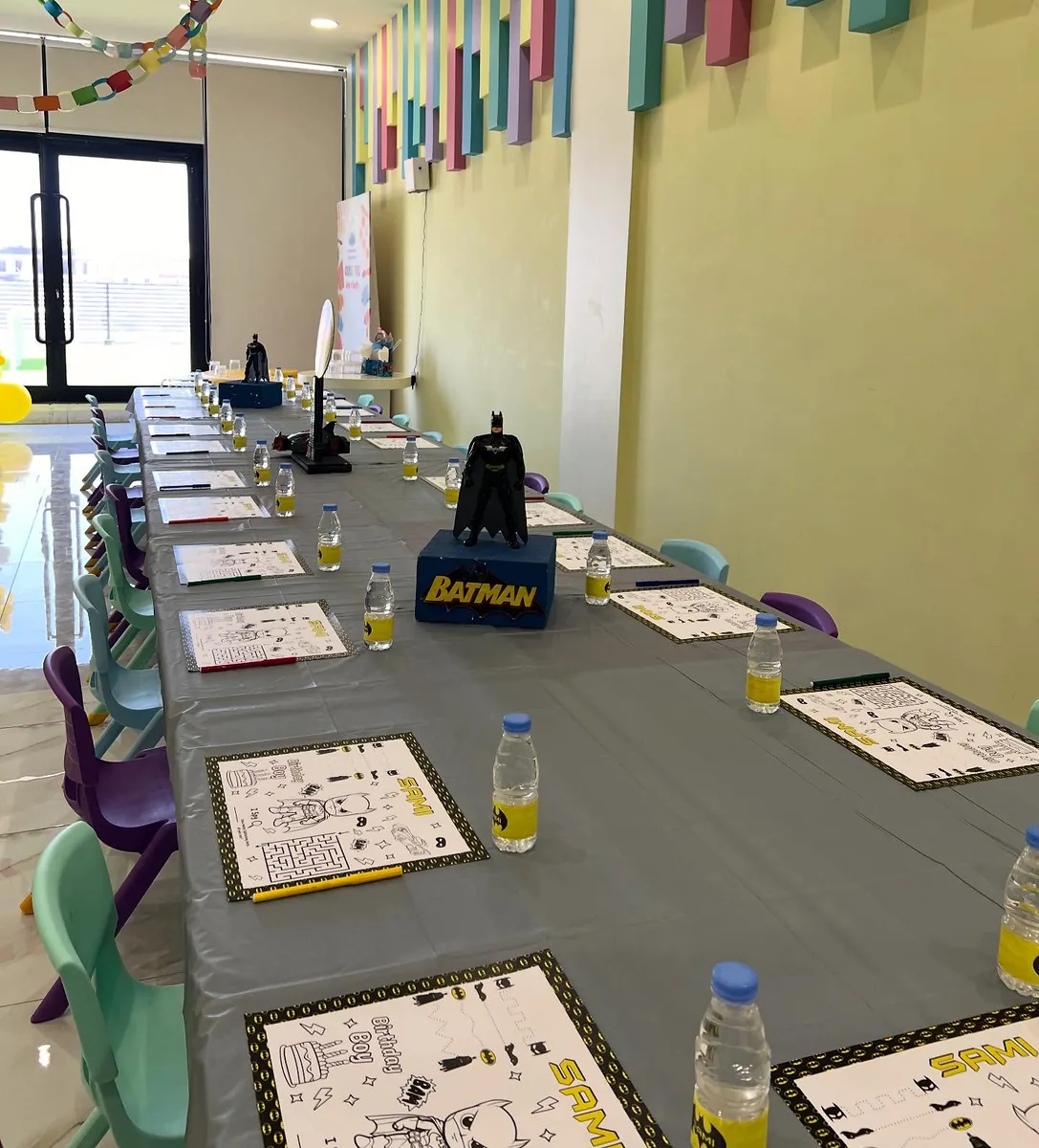 Long superhero party table with activity sheets, drinks and a central character prop